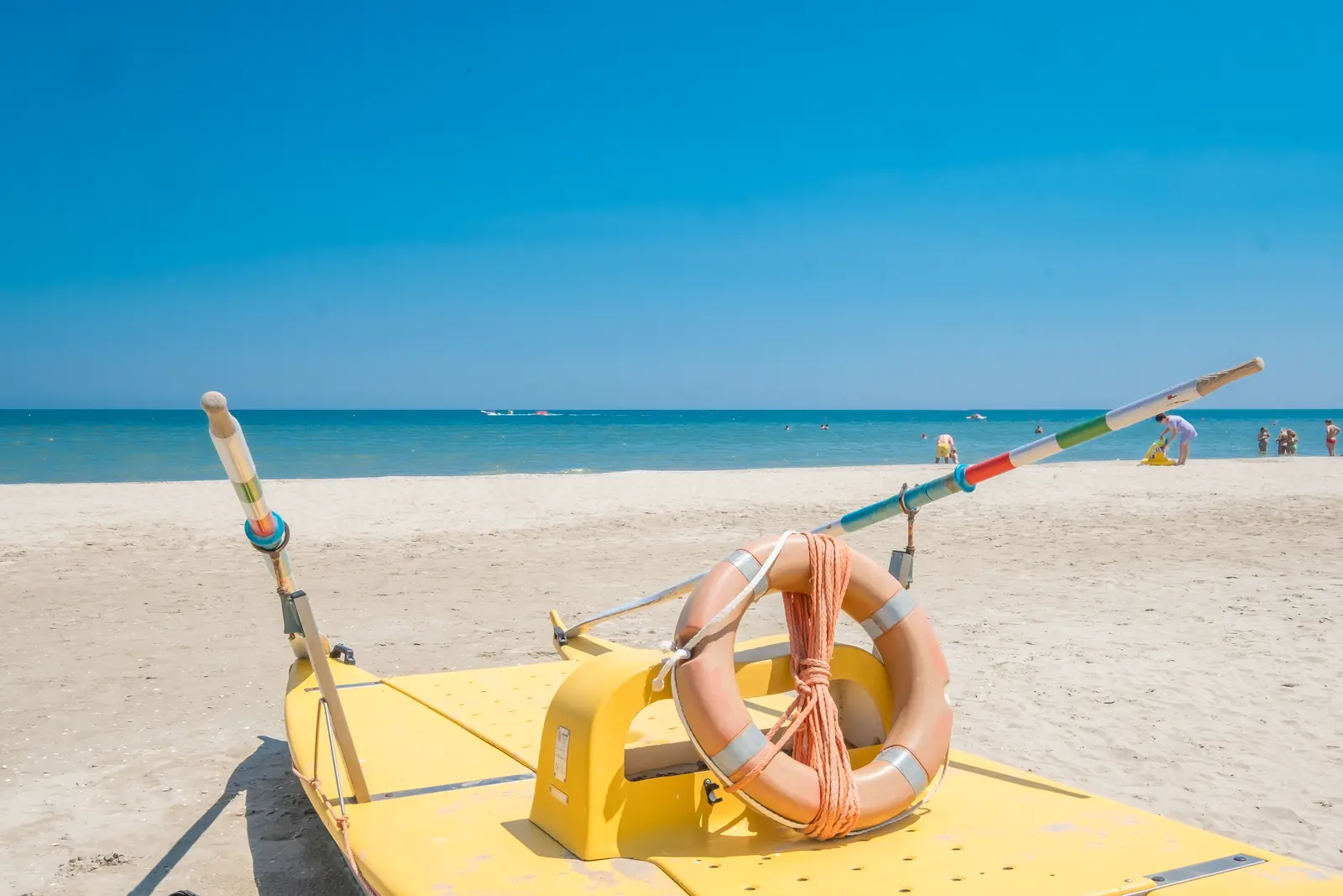 Un pattino giallo con i remi e un salvagente arancione sulla spiaggia di Riccione, davanti al mare calmo