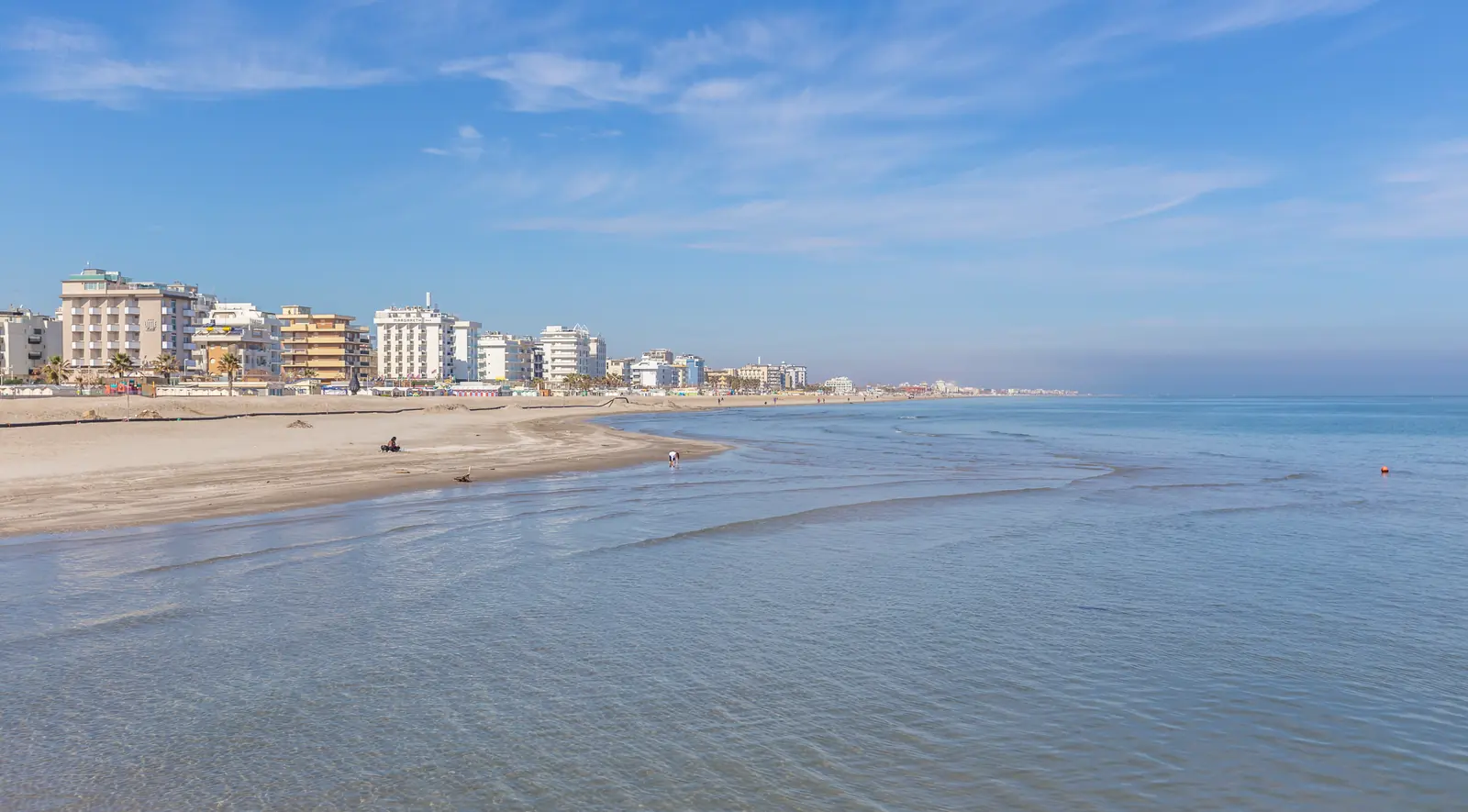 La spiaggia di Riccione fuori stagione, con il mare basso e calmo sulla battigia e la fila di alberghi lungo la costa