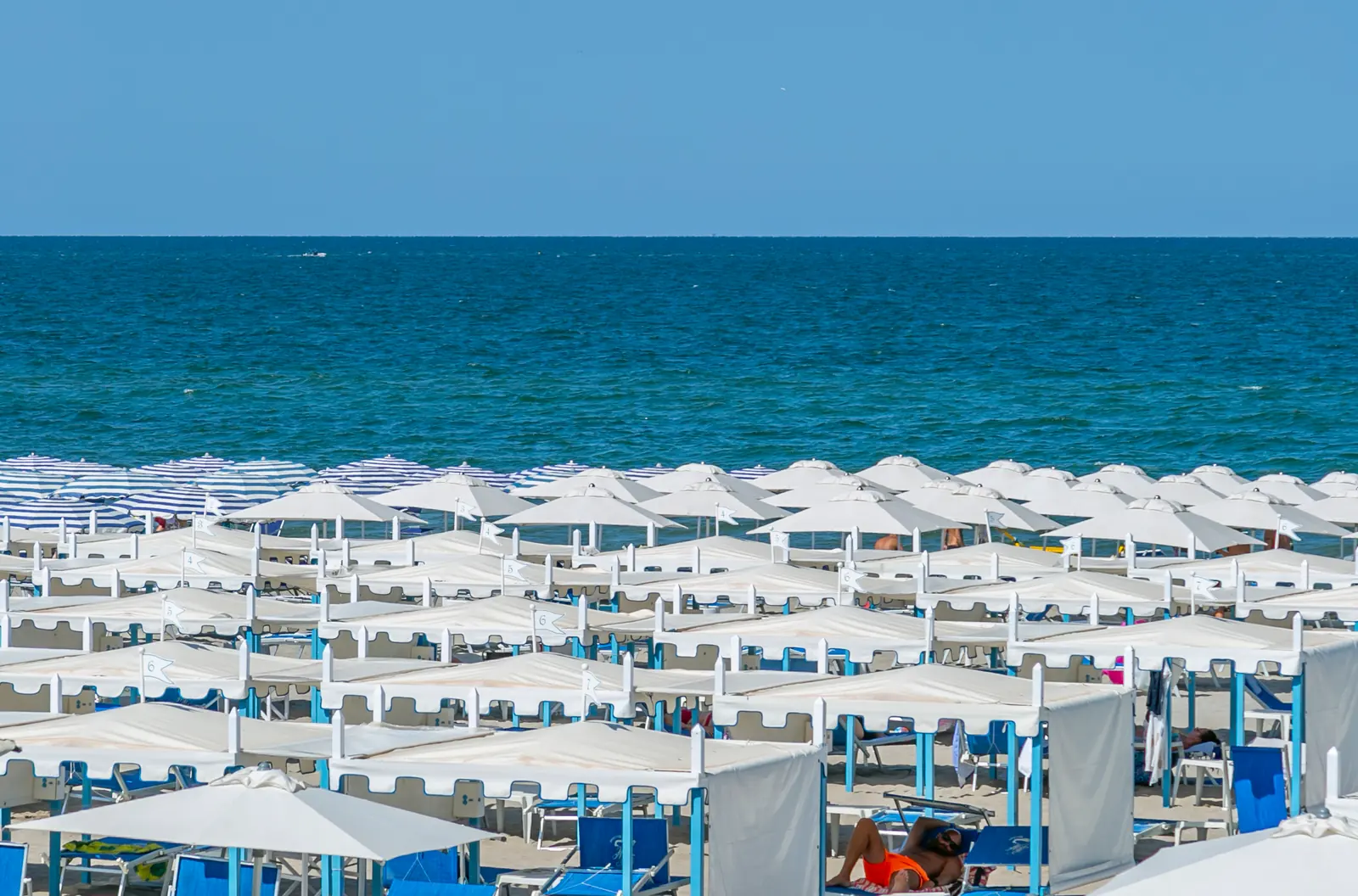 File ordinate di ombrelloni bianchi sulla spiaggia di Riccione viste dall'alto, con il mare azzurro in fondo