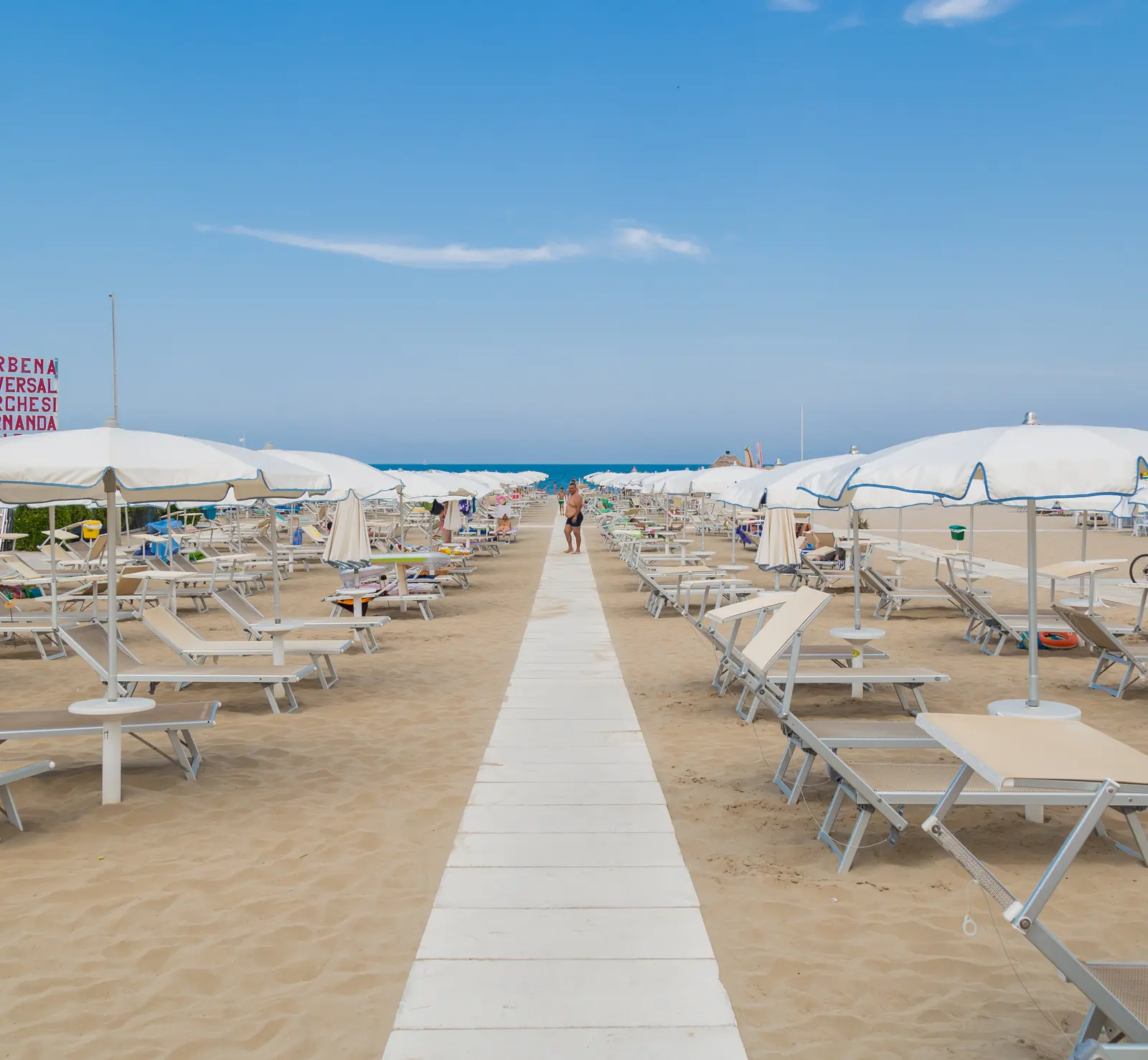 Una passerella bianca fra le file di ombrelloni bianchi e di lettini sulla spiaggia di Riccione Terme, verso il mare
