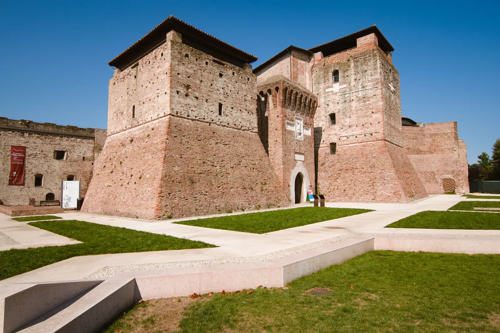 Castel Sismondo a Rimini di giorno, con le torri in mattoni, il portale e i prati della piazza davanti