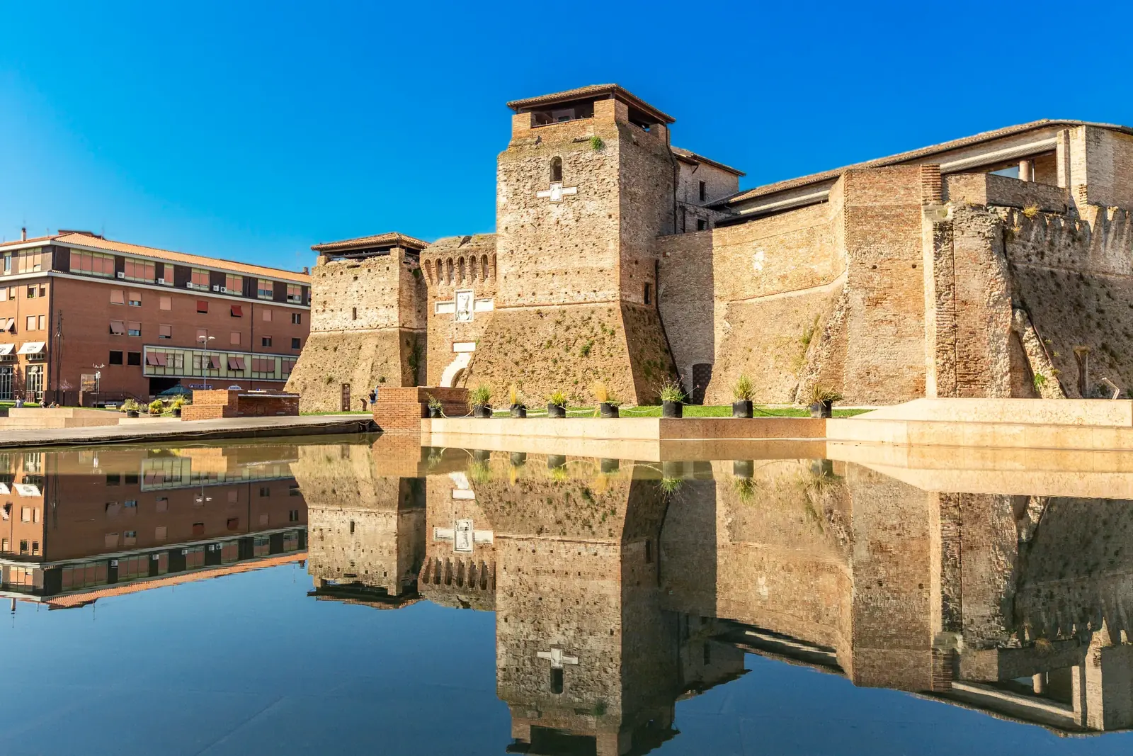 Castel Sismondo riflesso nella vasca d'acqua di piazza Malatesta, sotto il cielo azzurro