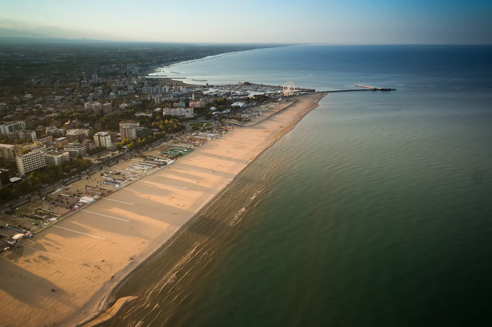 La costa di Rimini dall'alto all'alba, con la lunga spiaggia, il porto e la ruota panoramica in lontananza
