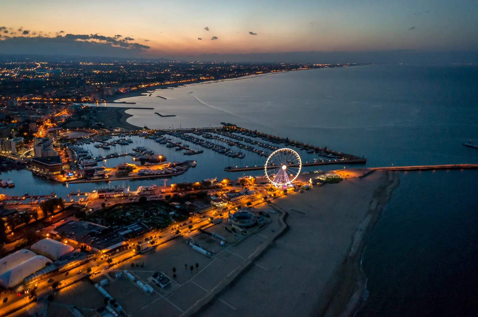 Rimini di sera vista dall'alto, con la darsena, la ruota panoramica illuminata e il lungomare