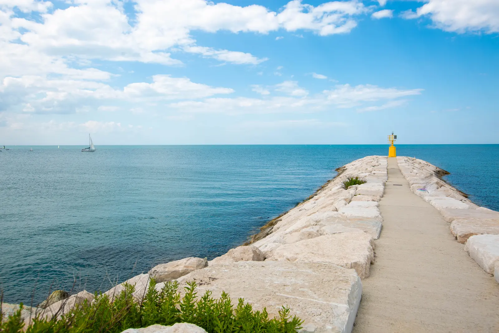 Il molo di Rimini fra i massi chiari, con il fanale giallo in fondo e il mare azzurro