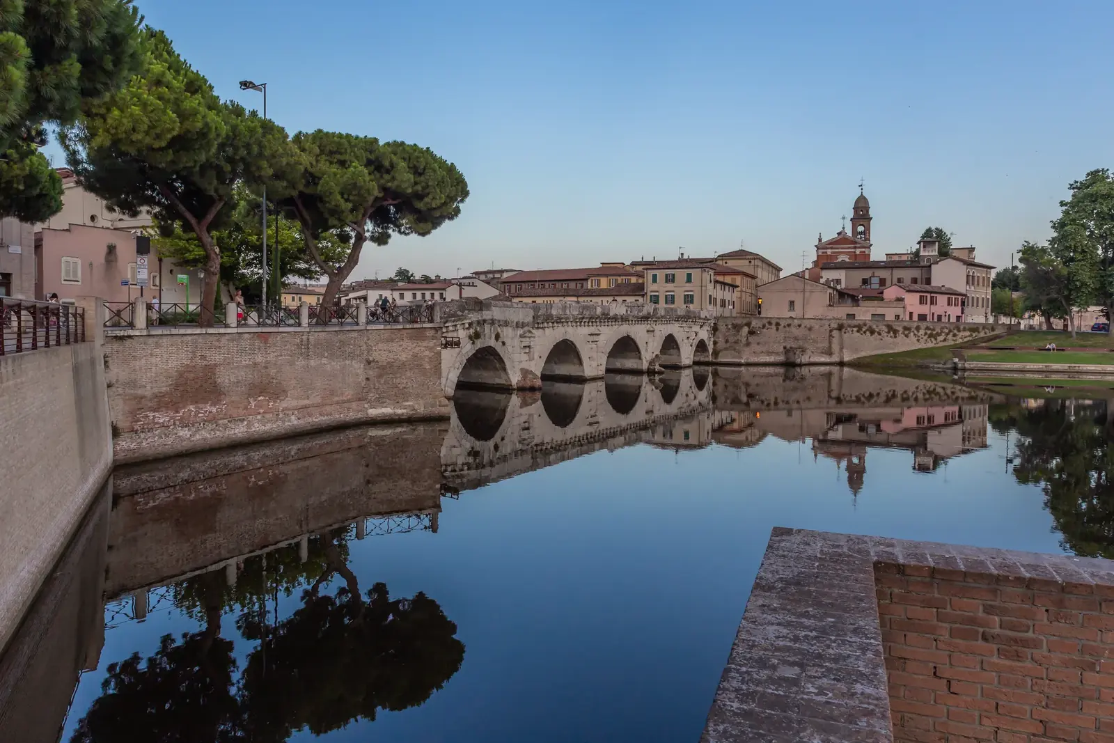 Il Ponte di Tiberio al crepuscolo, riflesso nell'acqua dell'invaso, con le case di Borgo San Giuliano e un campanile