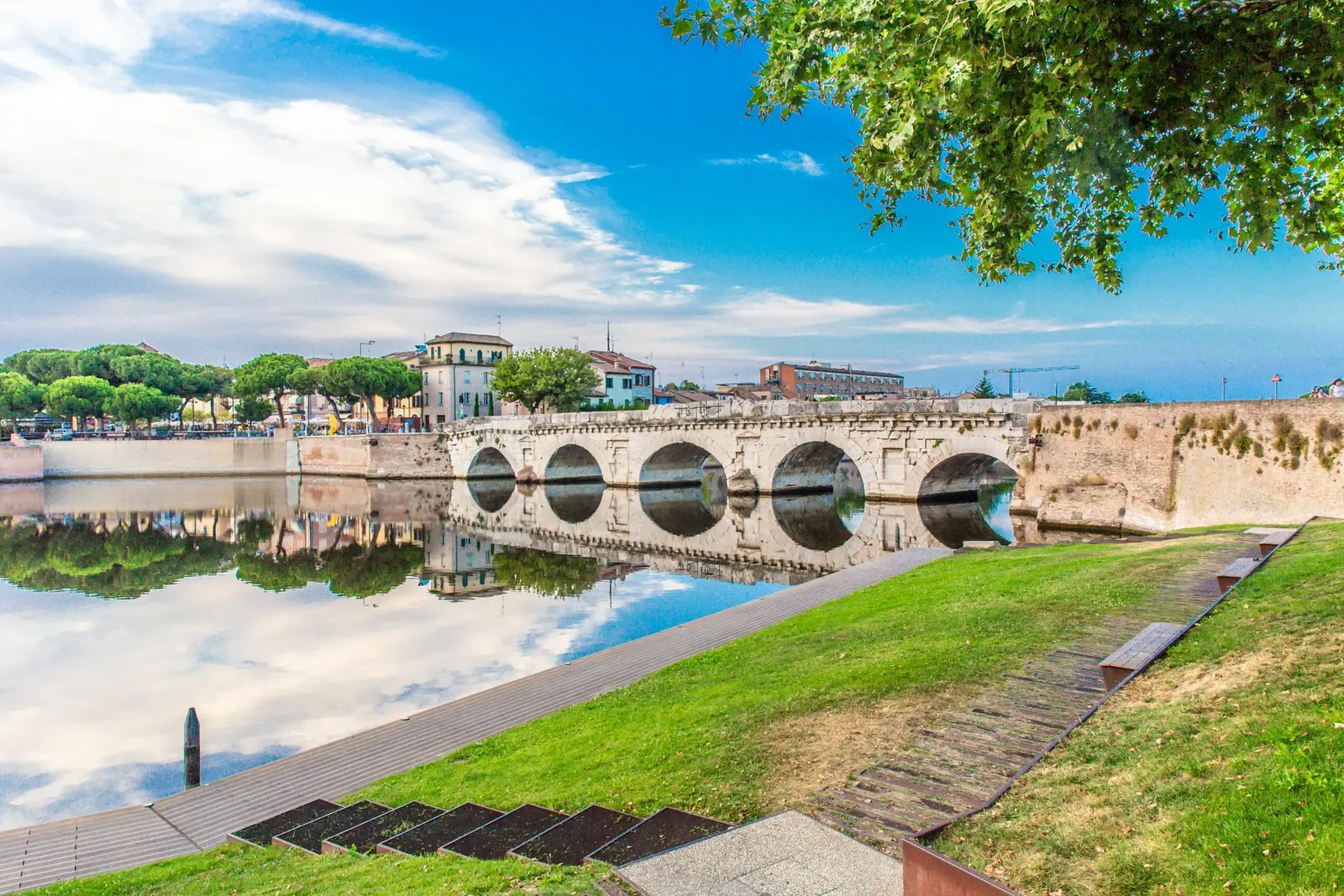 Il Ponte di Tiberio riflesso nell'invaso del Marecchia, con il prato e le gradinate della riva in primo piano
