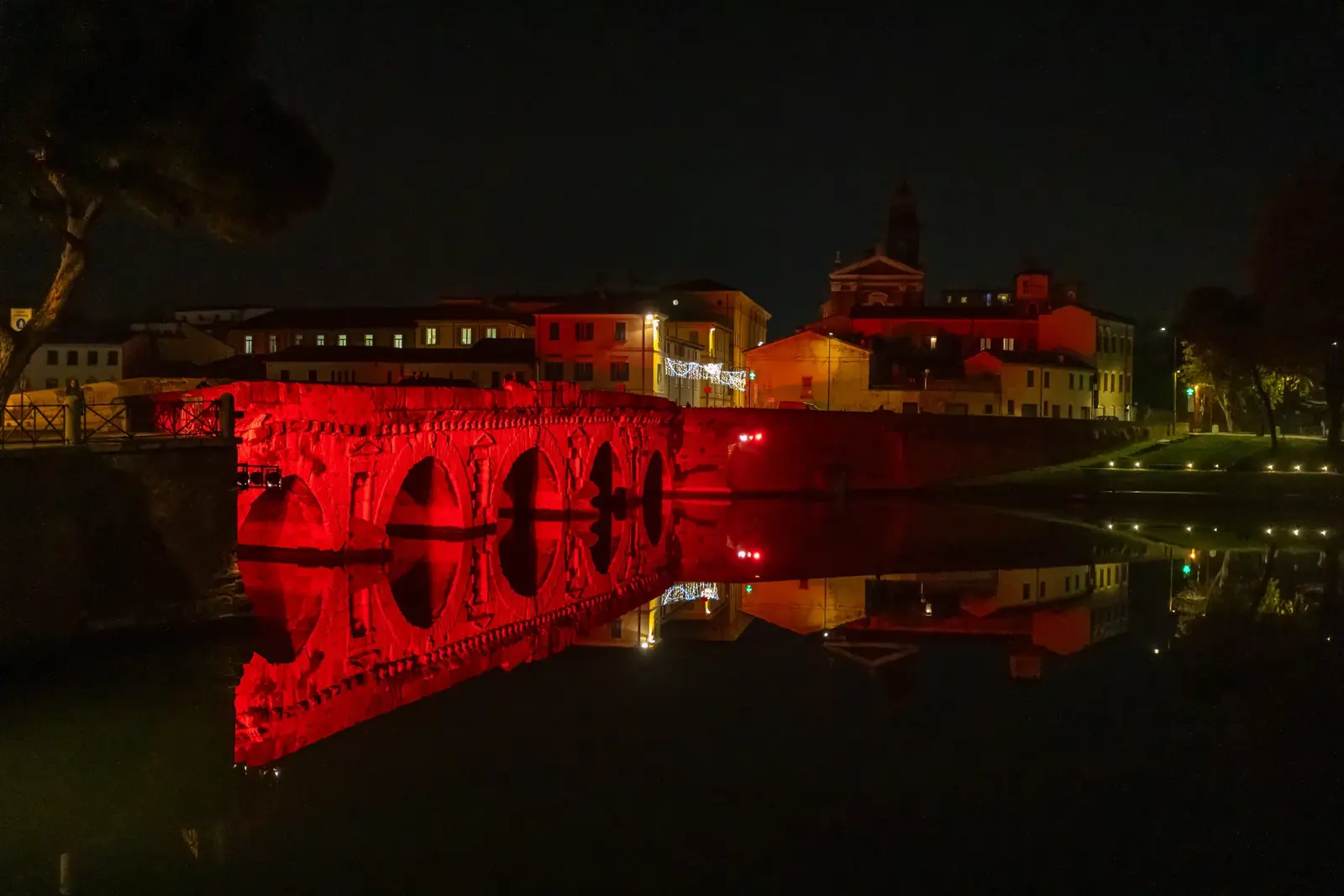 Il Ponte di Tiberio di sera, illuminato di rosso e riflesso nell'acqua scura dell'invaso
