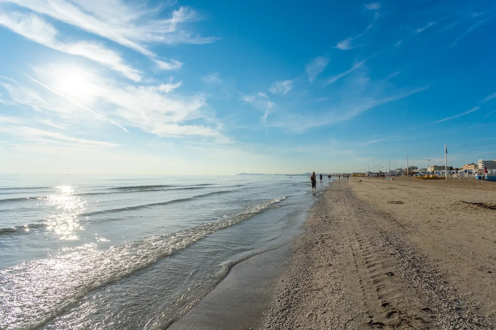 La riva di Rimini quasi deserta al mattino, con il sole basso, l'acqua bassa e le orme sulla sabbia