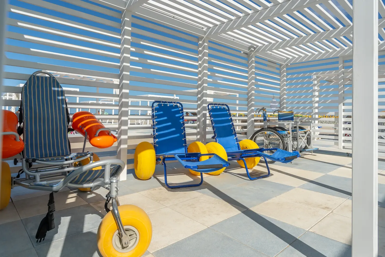 Le sedie da spiaggia con le ruote larghe per le persone con disabilità, sotto una pergola della spiaggia libera di Rimini