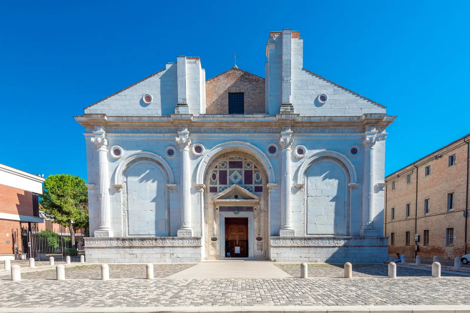 La facciata in pietra bianca del Tempio Malatestiano vista di fronte, con le colonne, gli archi e il portale centrale