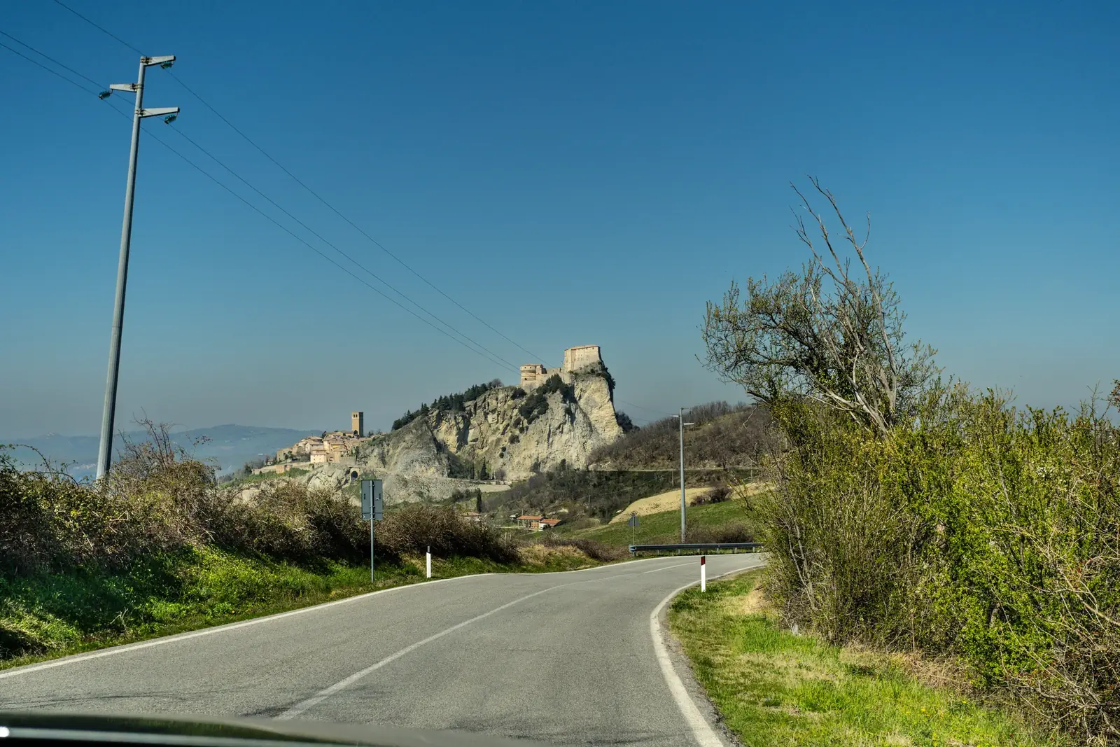 La rupe di San Leo con la fortezza in cima e il paese sul fianco, vista dalla strada che sale fra le colline